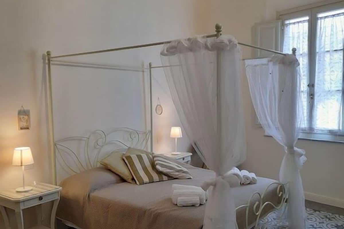 Ein Bett mit Himmelbett, ein Nachttisch mit Lampe und ein Fenster mit Vorhängen.