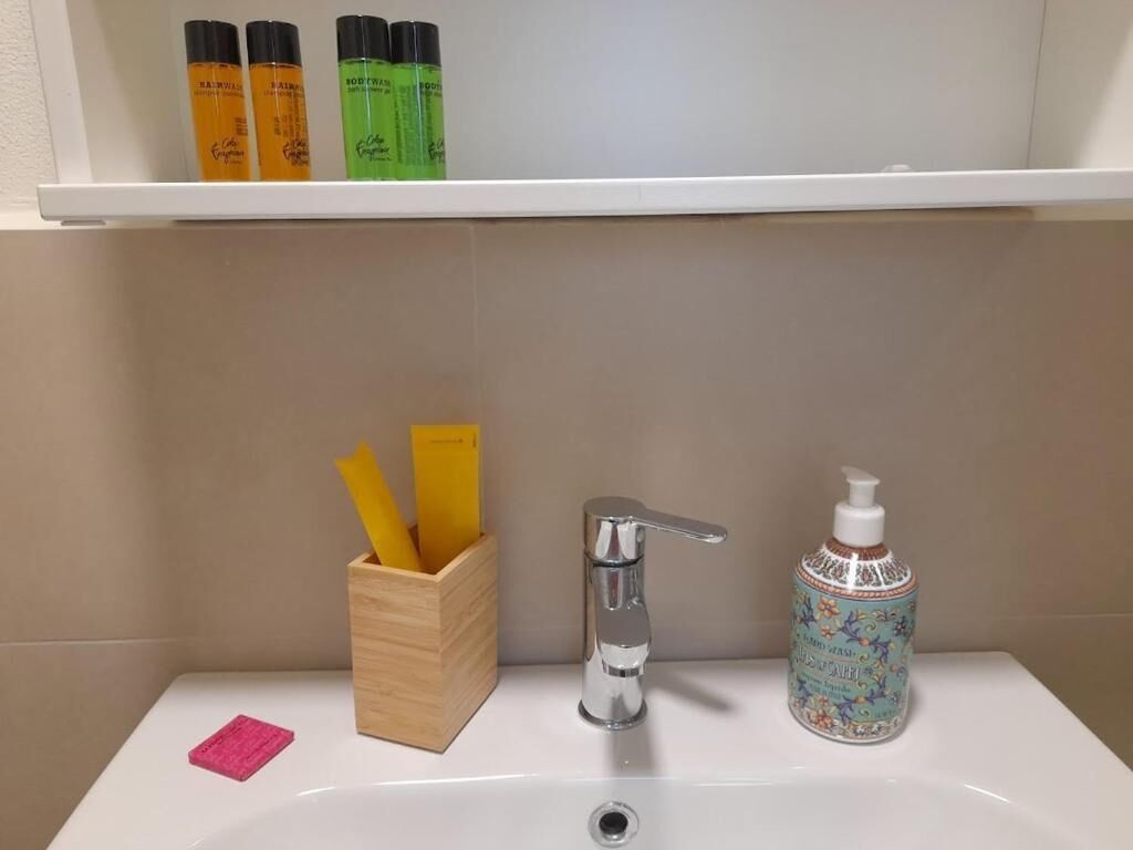 A bathroom sink with a chrome faucet, a wooden container holding yellow and green bottles, and a decorative bottle of hand soap.