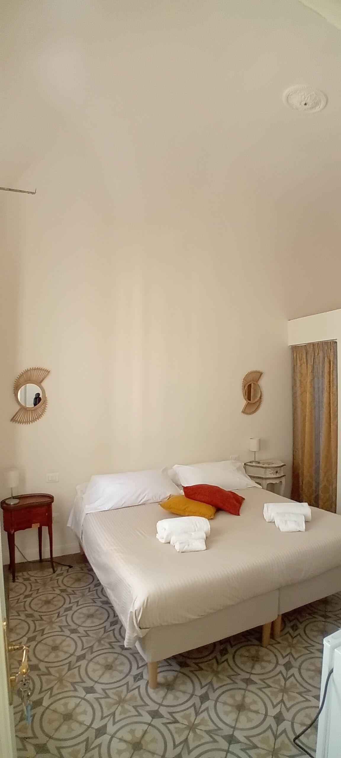 A hotel room with a bed, a nightstand, a mirror, and a patterned floor.