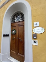 Puerta doble de madera con un ventanal decorativo encima, un cartel con el número '4' y una placa con el nombre 'Villino Luschi'.