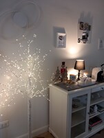 Una habitación con un armario blanco, un pequeño árbol de Navidad con luces, una lámpara y un letrero en la pared que indica Wi-Fi gratuito.