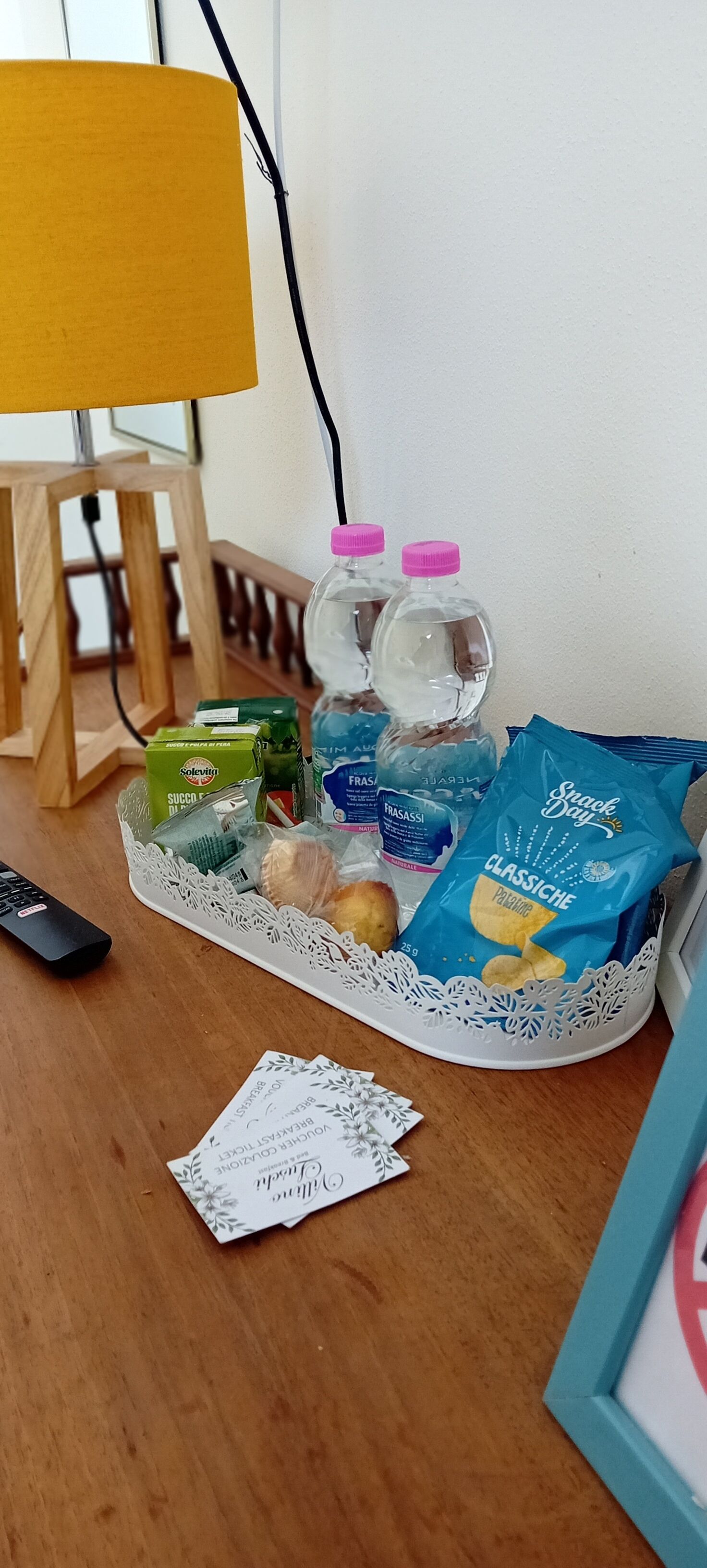 A tray with snacks, drinks, and a remote control on a wooden table.