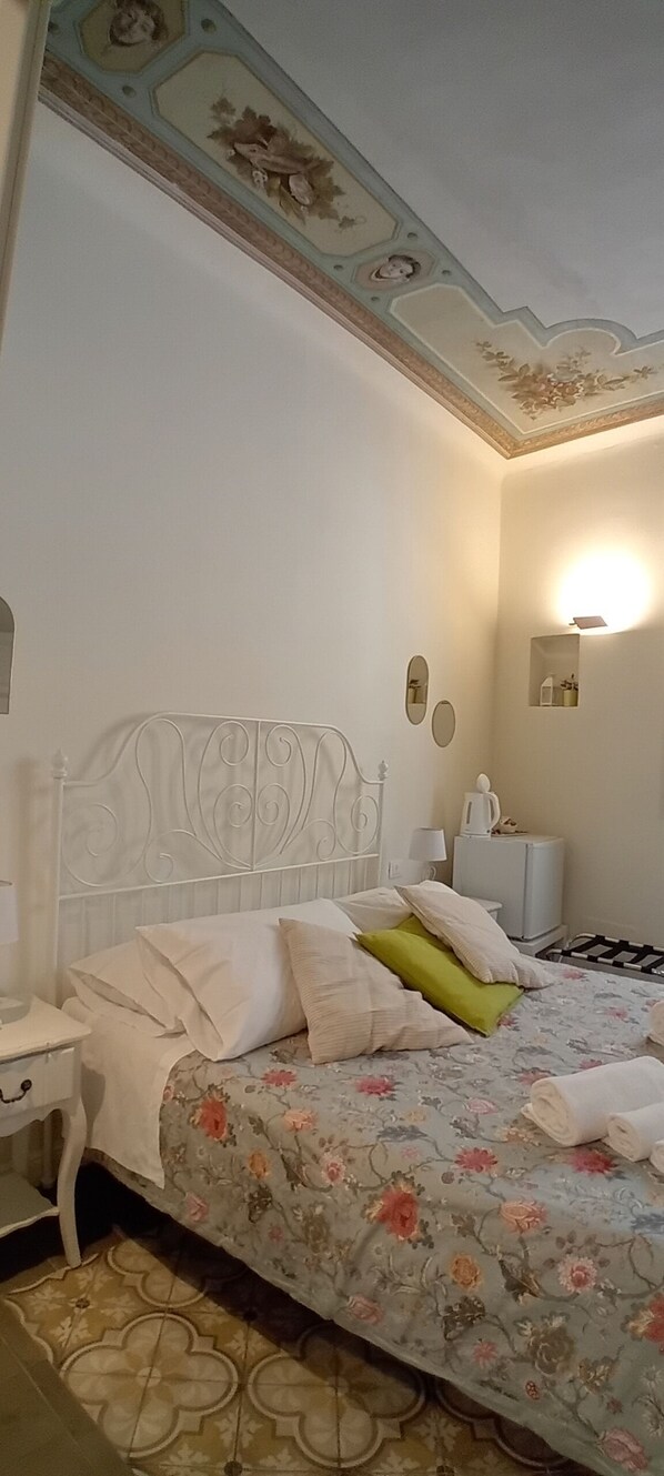 A bedroom with a floral bedspread, a white metal headboard, a bedside table with a lamp, and a nightstand. - B&B Villino Luschi Pisa Centro (Pisa)