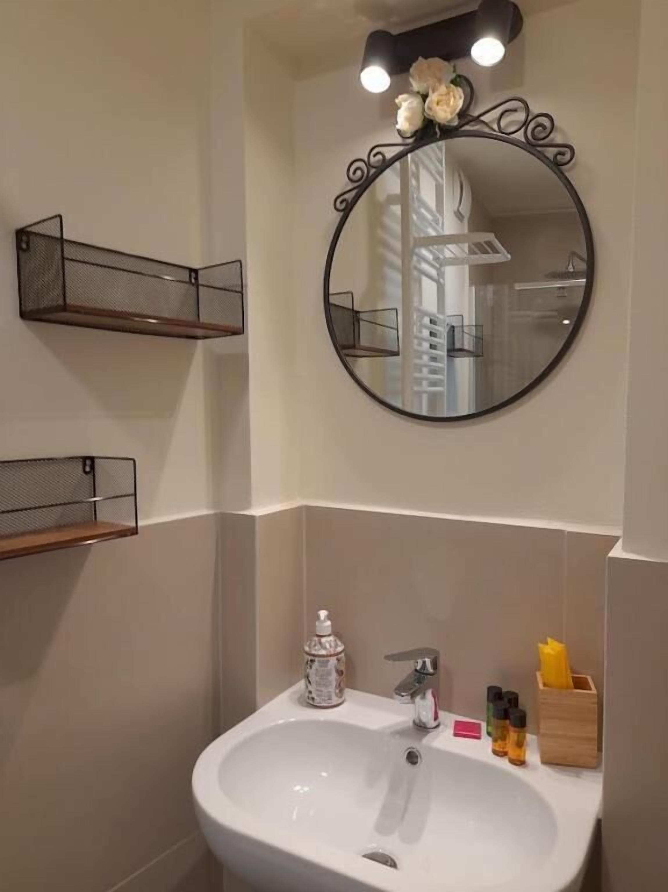 A bathroom with a white sink, a round mirror, and a shelf with toiletries.
