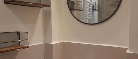 A bathroom with a white sink, a round mirror, and a shelf with toiletries.