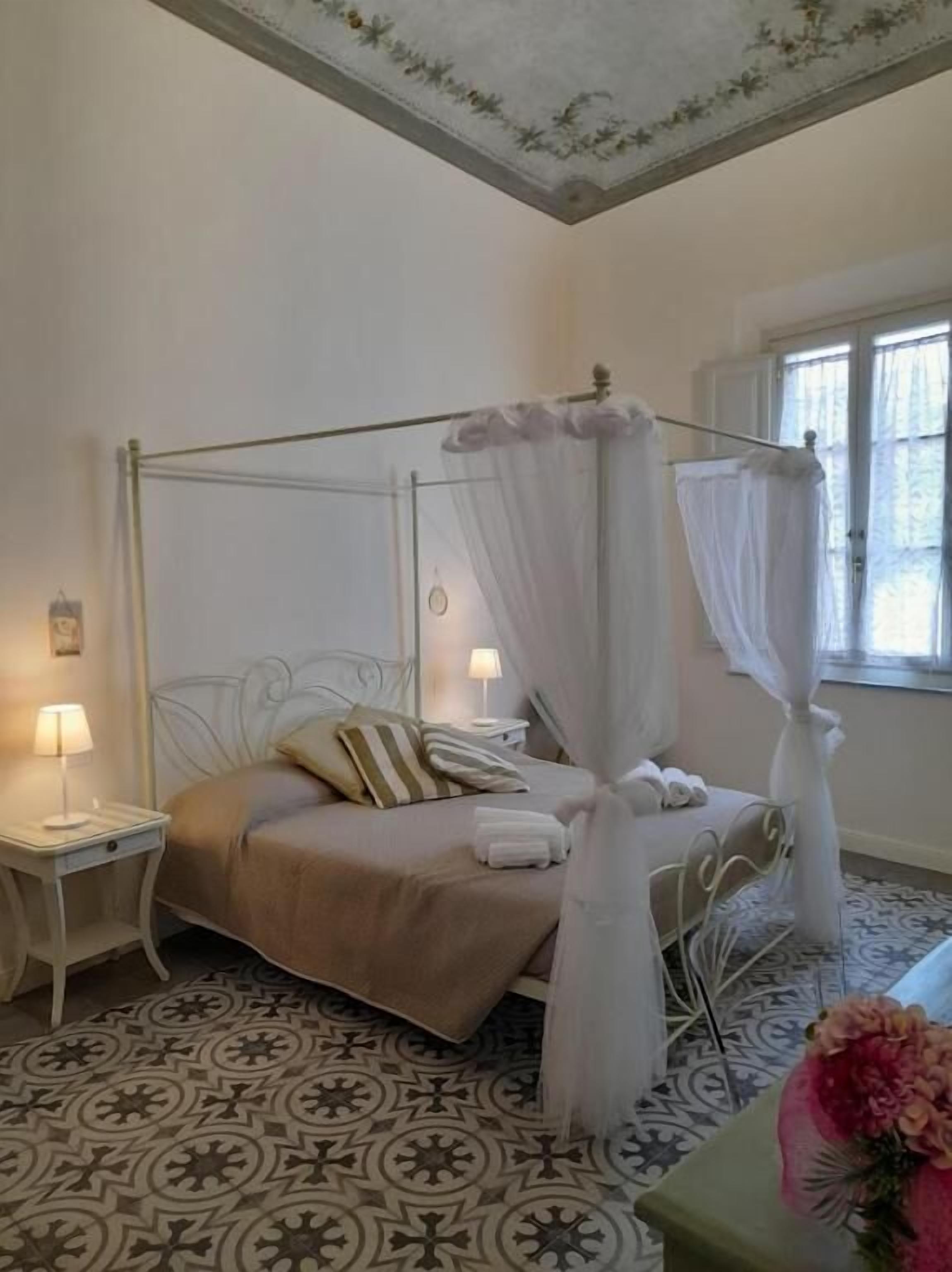 Un lit à baldaquin, deux tables de chevet avec des lampes, un sol à motifs et une fenêtre avec des rideaux.
