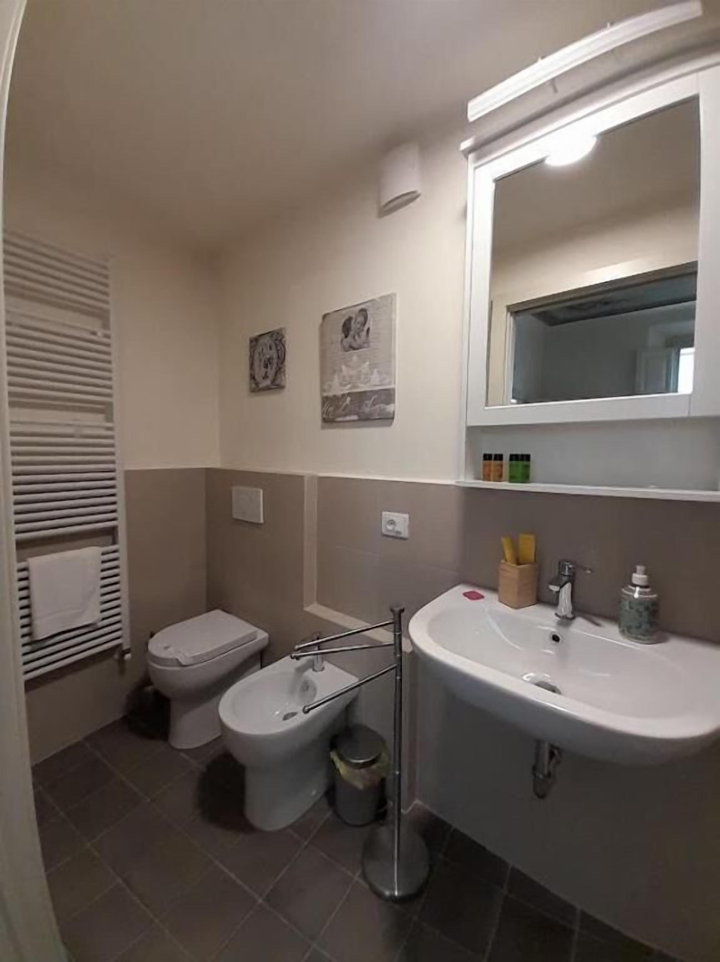 Ein Badezimmer mit Toilette, Bidet und Waschbecken. Zwei Wandleuchten und ein Spiegel sind über dem Waschbecken angebracht.