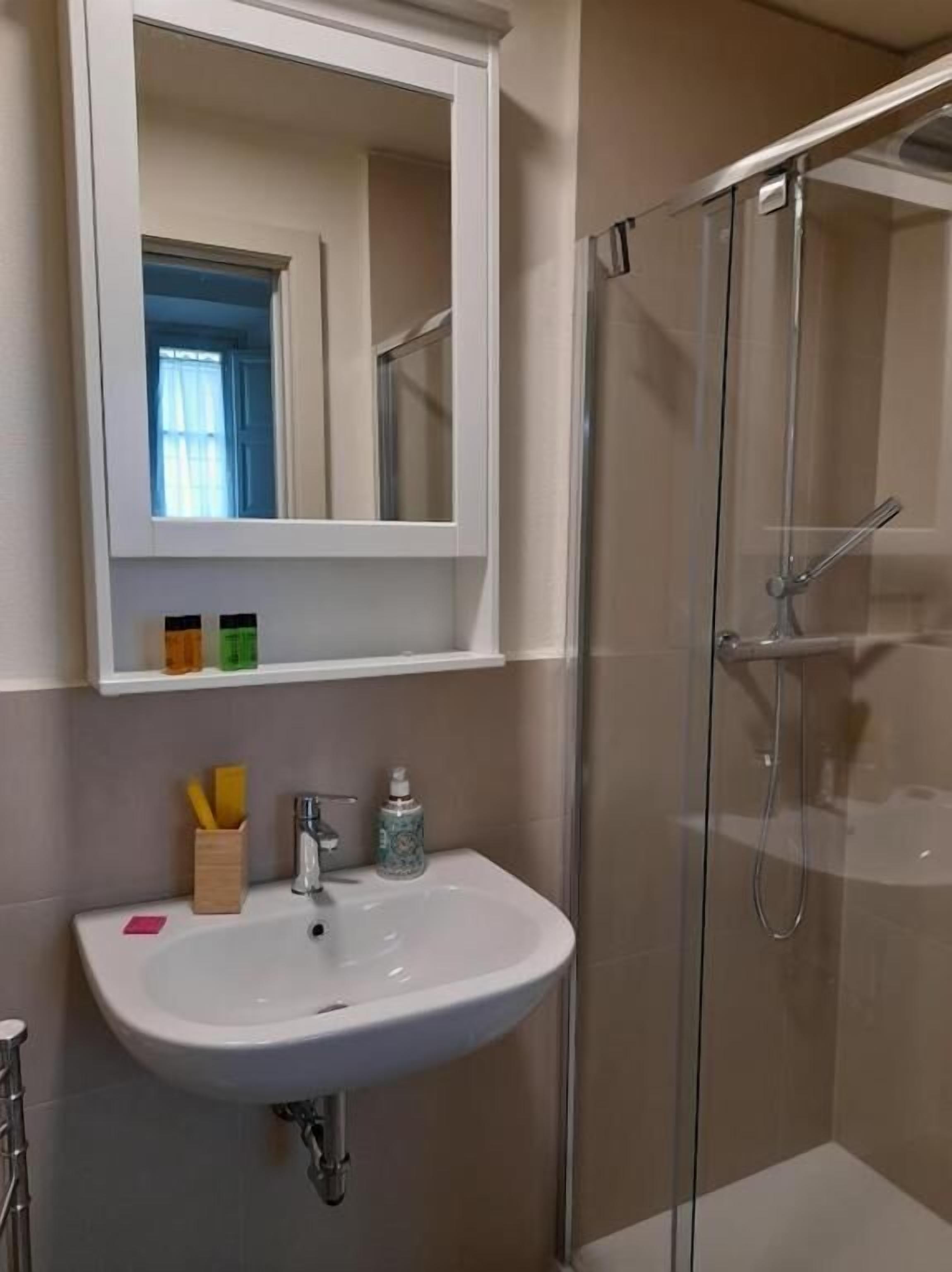 Un baño con lavamanos blanco, un espejo y ducha con mampara de vidrio.