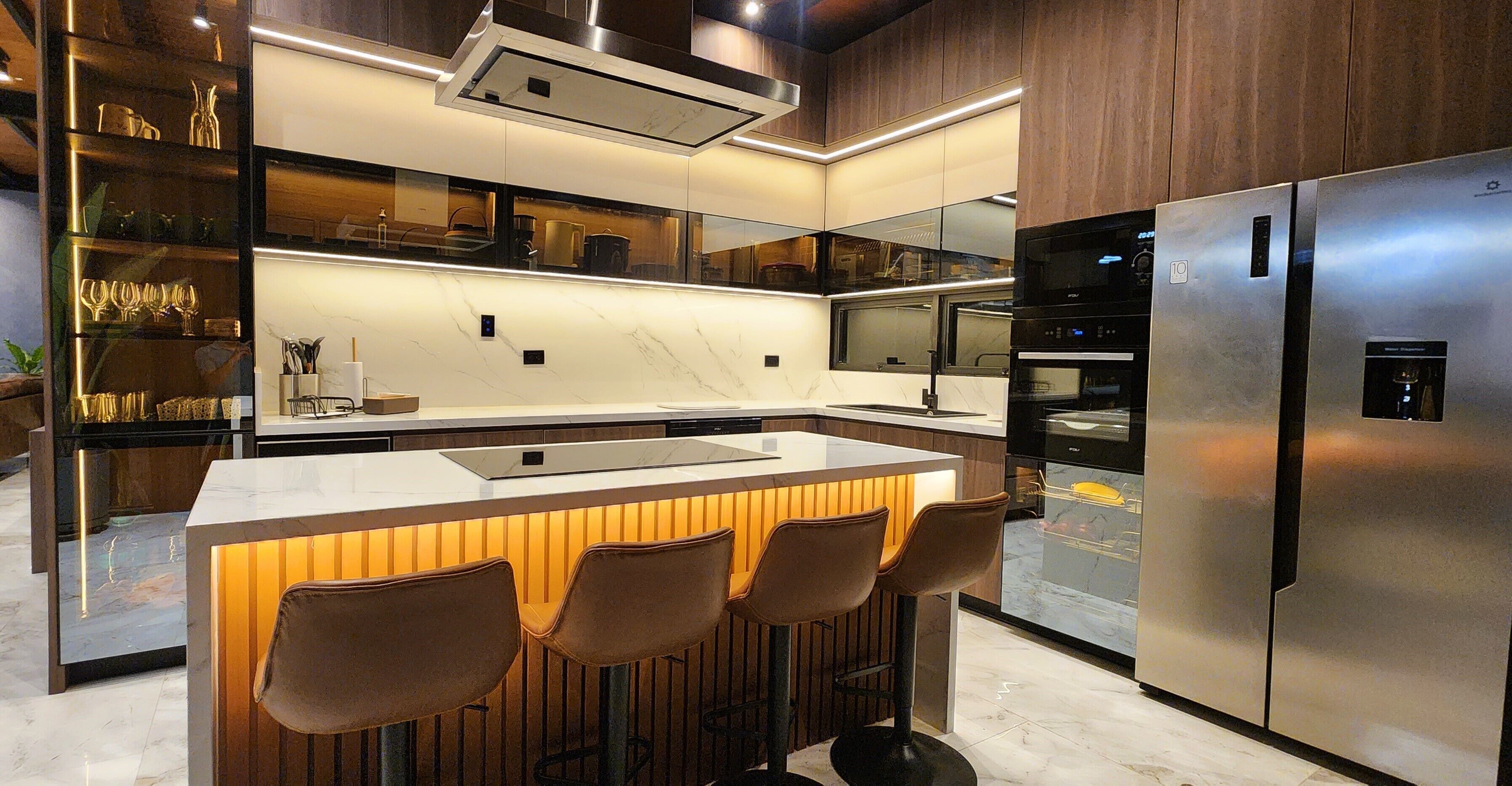 Une cuisine moderne dotée d’un îlot central, de tabourets de bar, d’appareils électroménagers en acier inoxydable et d’un dosseret en marbre.