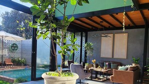 Un espacio interior moderno con un amplio ventanal, una planta en maceta y una piscina visible a través del vidrio.