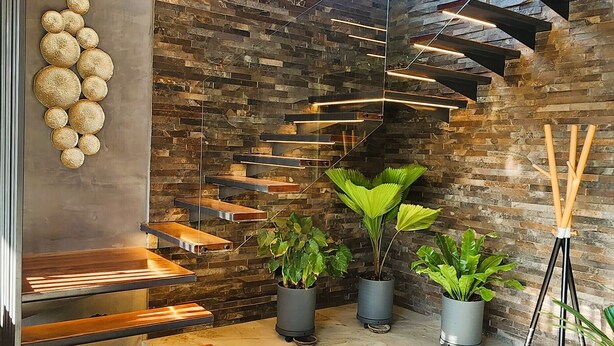 Un interior moderno con techo de madera, pared de piedra y escalera con jardineras integradas.
