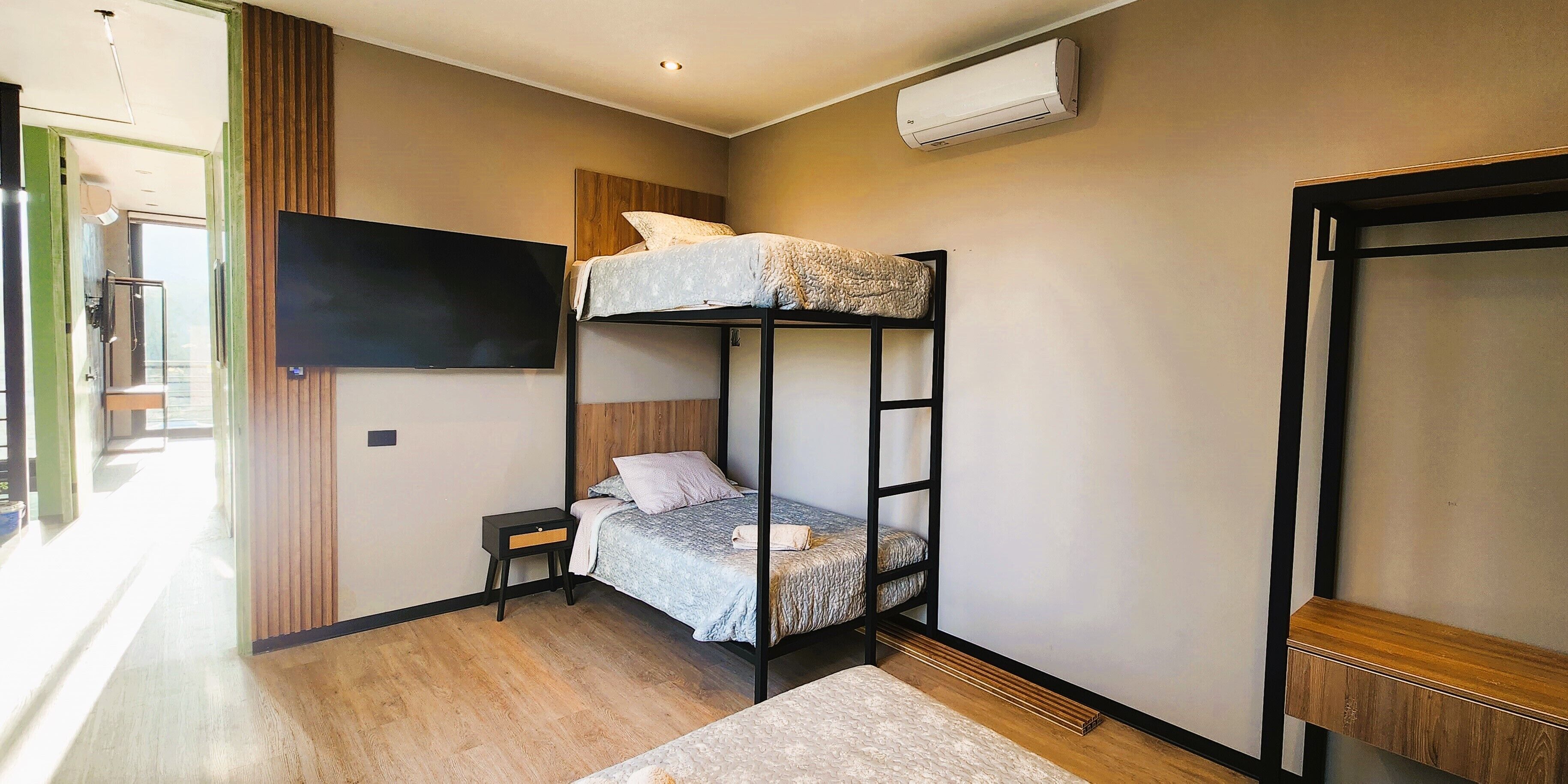 Habitación con literas, un televisor montado en la pared, una mesita de noche pequeña y suelo de madera.