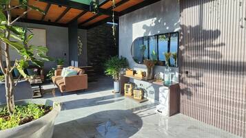 Uma área de estar externa moderna com parede de pedra, teto de madeira e um espelho grande refletindo o ambiente.