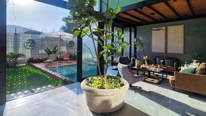 Una sala de estar moderna con un ventanal grande, una planta en maceta, una piscina y mobiliario de exterior.