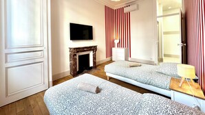 Ett modernt hotellrum med en öppen spis, en platt-TV, en säng med mönstrat sänglinne och en spegel som reflekterar rummet.