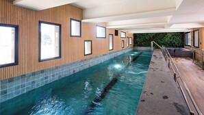 Una piscina con pared de madera y suelo de baldosas, rodeada de ventanas y barandilla de metal.