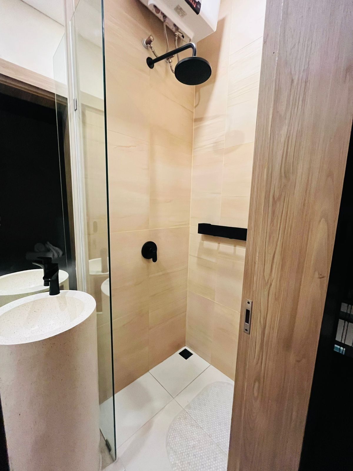 A modern bathroom with a glass shower enclosure, a white sink, and a black towel rack.
