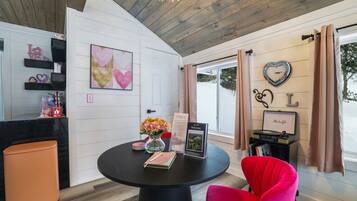 Una habitación moderna con una mesa redonda, una silla roja, un florero con flores, un cartel de bienvenida y una pared con un adorno con forma de corazón.