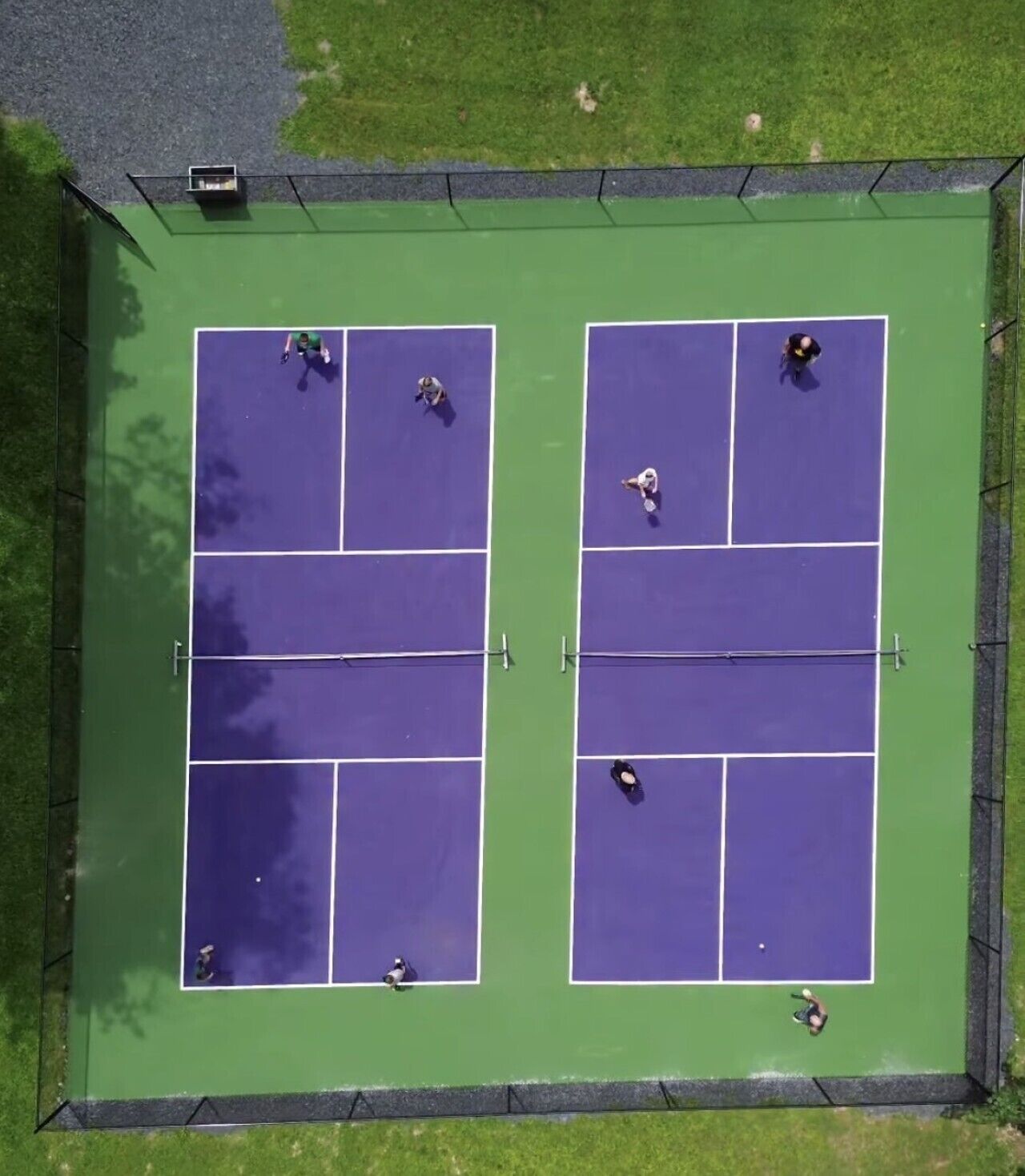 Luftaufnahme eines Tennisplatzes mit vier Spielern, umgeben von einem grünen Zaun.