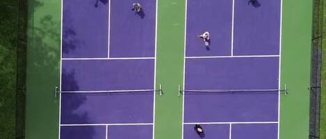 Luftaufnahme eines Tennisplatzes mit vier Spielern, umgeben von einem grünen Zaun.