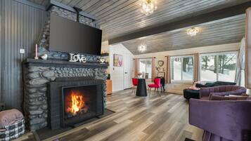 A cozy living room with a stone fireplace, wooden ceiling, and large windows.