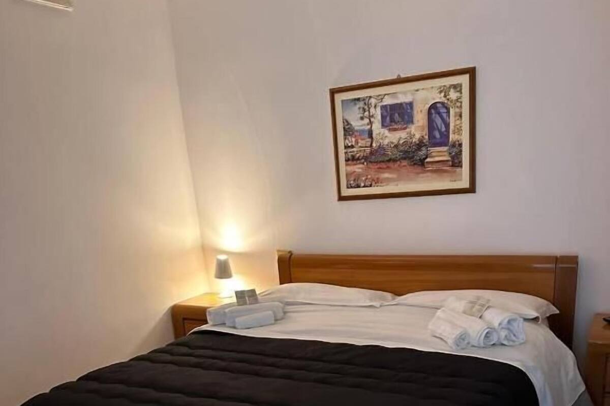A single bed with a wooden frame, a white and black duvet, and a bedside table with a lamp.