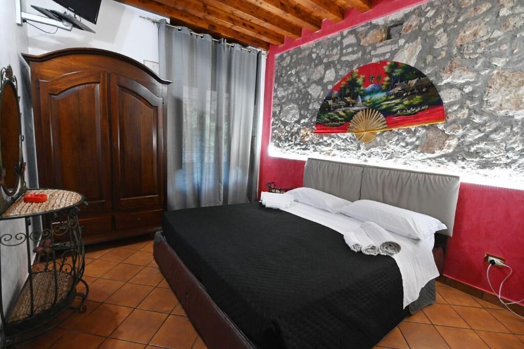 Une chambre à coucher comprenant un lit, une armoire en bois, une petite table avec un panier, et un mur orné d’un éventail décoratif.