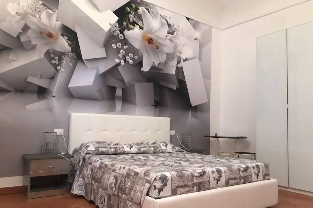 A bedroom with a bed, nightstand, and a wall with a floral design.