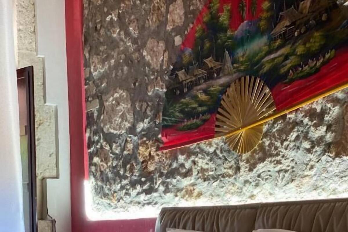 A hotel room with a bed, pillows, a blanket, a painting, and a window.
