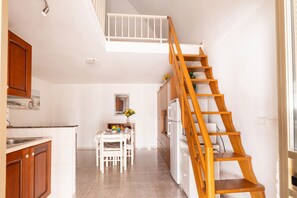 Eine Küche mit Holzausstattung, einem Esstisch mit Stühlen, einer weißen Treppe und einem kleinen Fenster.