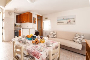 Ein gemütlicher Wohnbereich mit einer Couch, einem Esstisch gedeckt mit Frühstücksleckereien und einer Küche im Hintergrund.