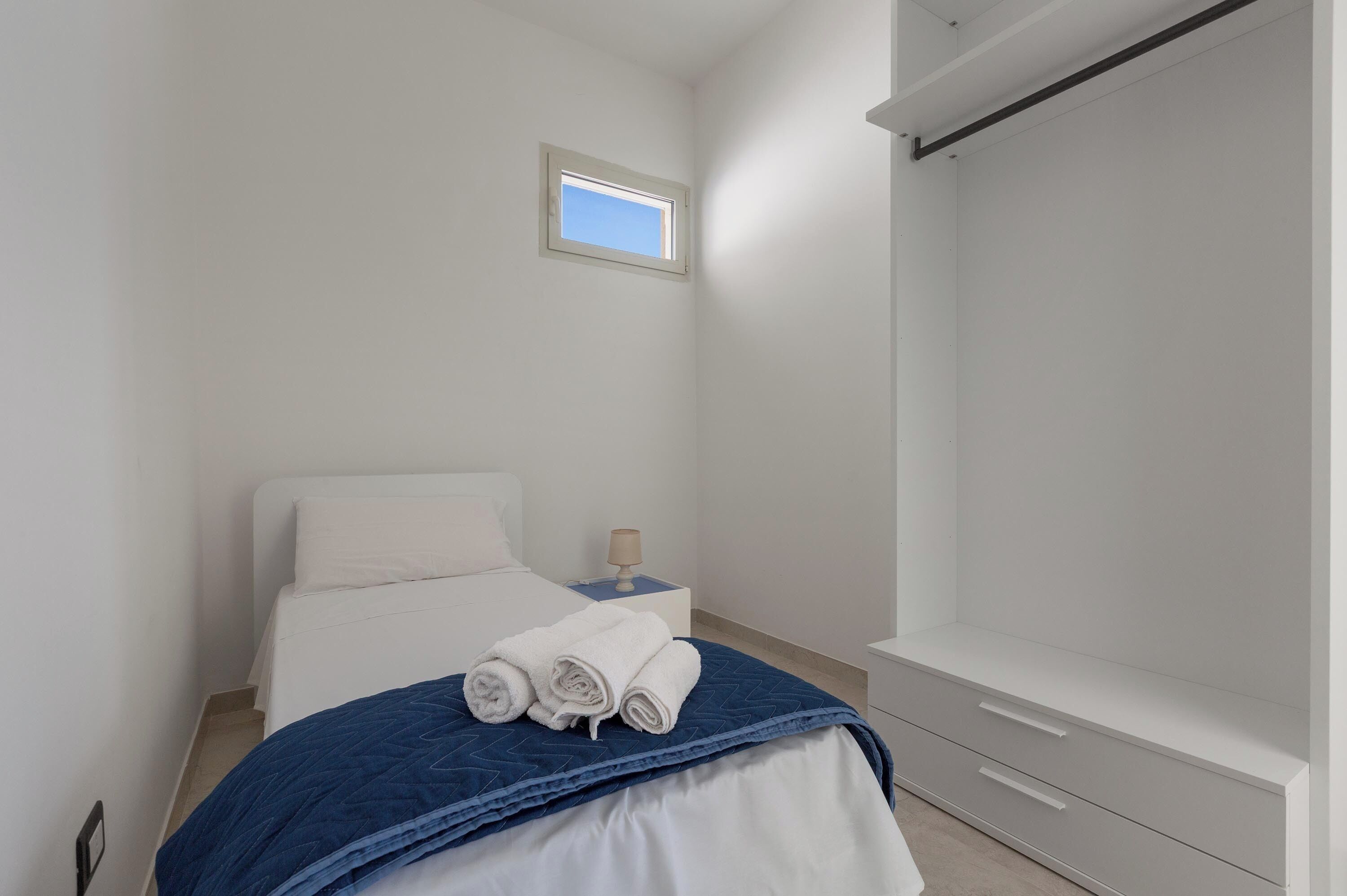 Un dormitorio con cama, mesita de noche, ventana y armario.