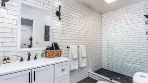 A bathroom with white subway tiles, a white sink with black faucets, a white toilet, and a black shower area. - Chic Yosemite Escape: King Suite w/ Plush Comforts (Oakhurst)