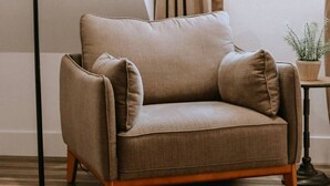 A beige armchair with wooden legs and two matching cushions, positioned on a striped floor. - Chic Yosemite Escape: King Suite w/ Plush Comforts (Oakhurst)