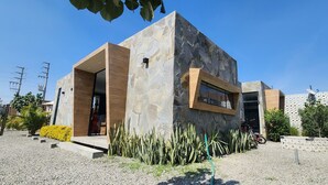 Ein modernes Gebäude mit Steinaußenwand, Holzeingang und einer kleinen Gartenanlage mit Kakteen und gelben Büschen.