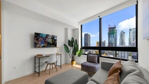 Un salón moderno con un ventanal grande, un escritorio, un sofá cómodo y una planta en maceta.