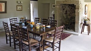 Un comedor con chimenea de piedra, sillas de madera y una mesa dispuesta para el desayuno.
