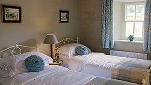 Un dormitorio con dos camas individuales, una mesita de noche con lámpara y una ventana con cortinas.