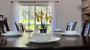 A dining table with a white bowl and saucer, two chairs, and a potted plant with yellow flowers. - New! Hillside | Valley View (Oakhurst)
