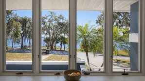 Habitación con un amplio ventanal que da a una zona ajardinada con árboles y una masa de agua.