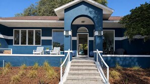 Una casa moderna con fachada azul, un porche cubierto con sillas y una escalera que conduce a la entrada.