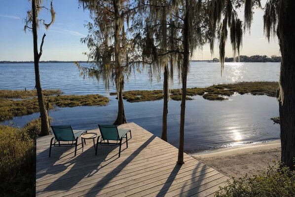 En träveranda med två stolar och ett bord, med utsikt över ett stilla vattenområde, omgiven av träd med spansk mossa.