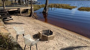 Una playa con una terraza de madera, sillas de descanso y una fogata.