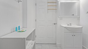 A white bathroom with a white sink, mirror, and door. There are toiletries on the counter.