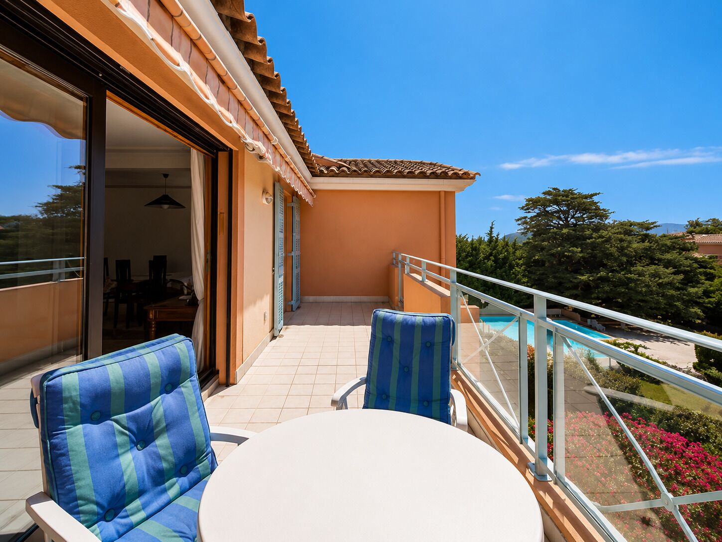 A balcony with a glass railing, a table, and two chairs with striped cushions.