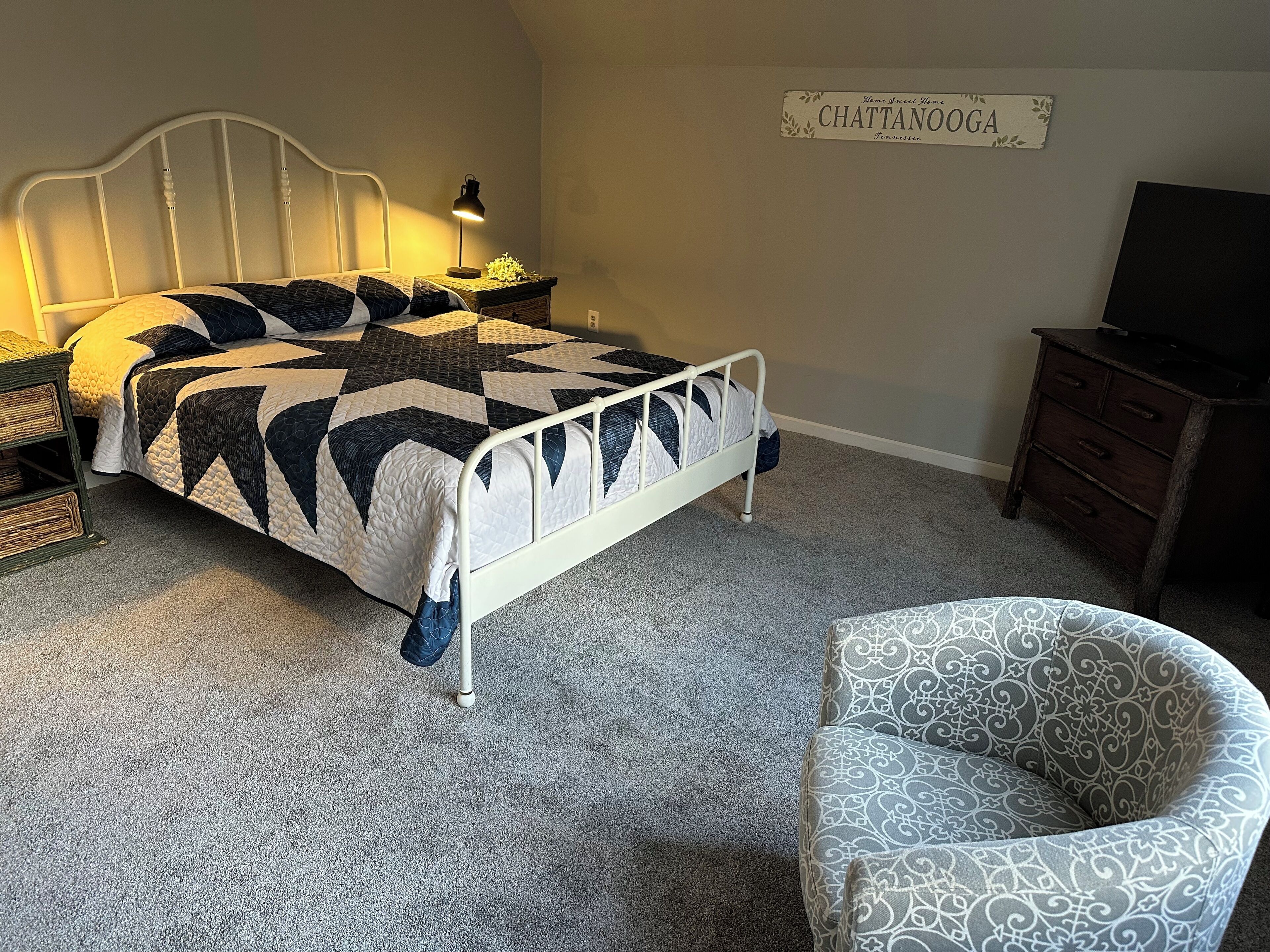 A bedroom with a bed, a nightstand, a lamp, a dresser, and a chair.