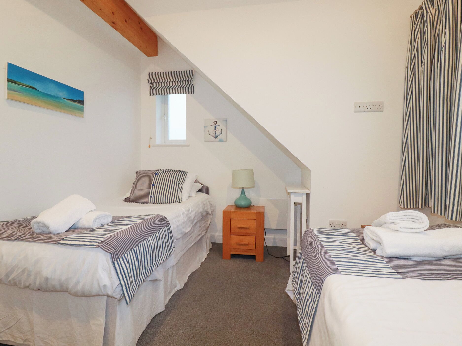 Un dormitorio con dos camas, una mesita de noche, una lámpara, una ventana con cortinas y un cuadro en la pared.