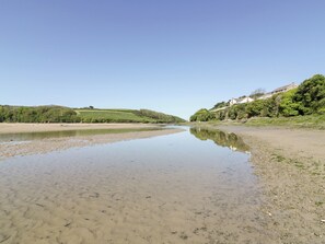 En flodbank med ett stilla vatten, en sandstrand och grönska på kullarna.