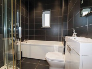 A modern bathroom with a bathtub, toilet, and glass shower enclosure. - Fistral Palms 2 (Newquay)