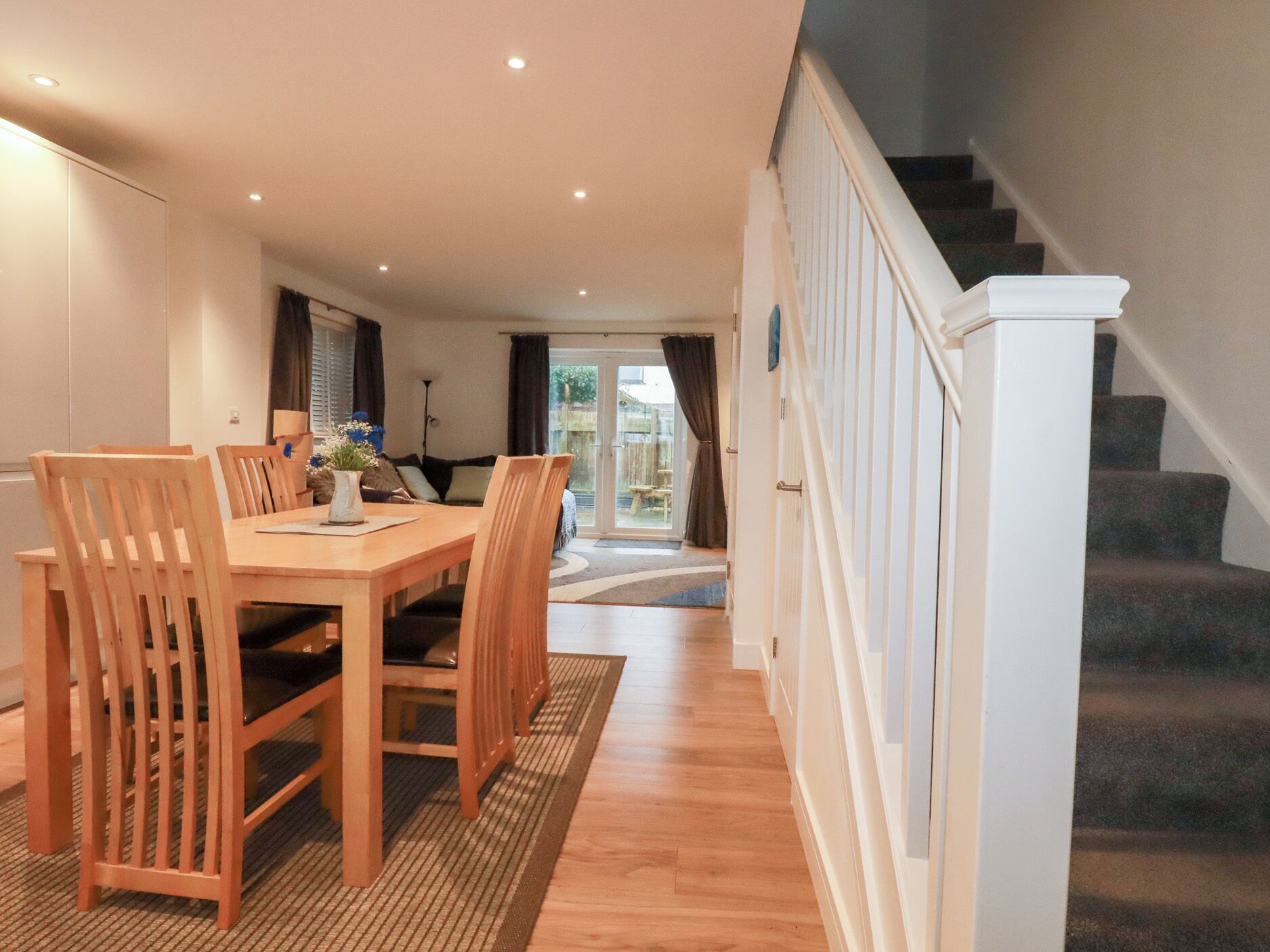 Un espace repas avec une table et des chaises en bois, un escalier et une vue sur l’extérieur.